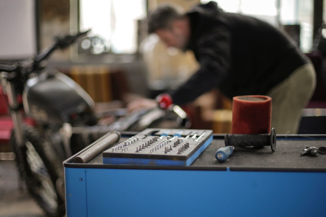 Plastic toolbox with small metal details placed on metal workbench in spacious garage while faceless adult male mechanic repairing motorbike